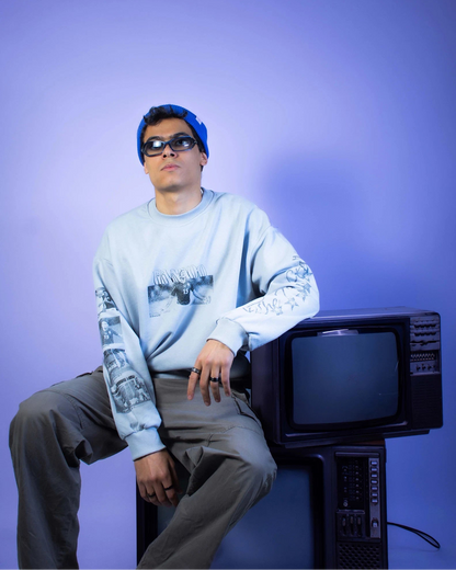 Person wearing a light gray sweatshirt with Gedo Football Player designs, sitting on an old television set against a purple background.