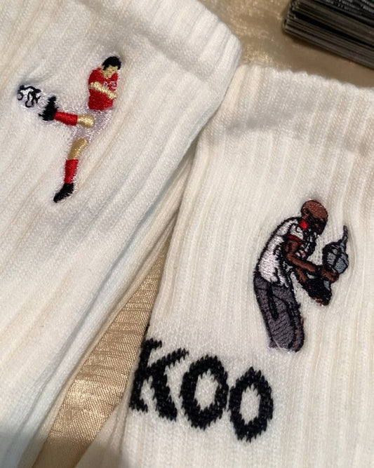 White crew socks with embroidered football players graphics and the brand name 'FANKOO' on the side, shown on a tabletop with cards in the background.